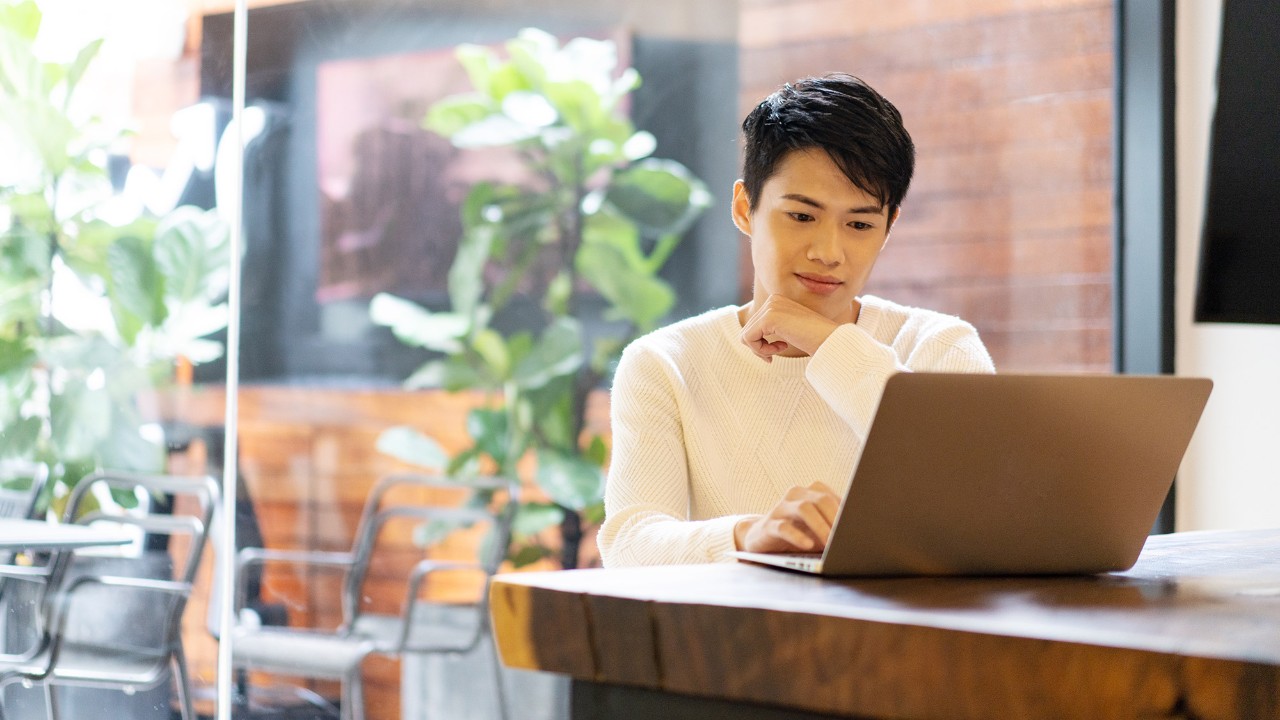 A man is using laptop in a coffee shop; image used for "beware of scams and fraud" article.