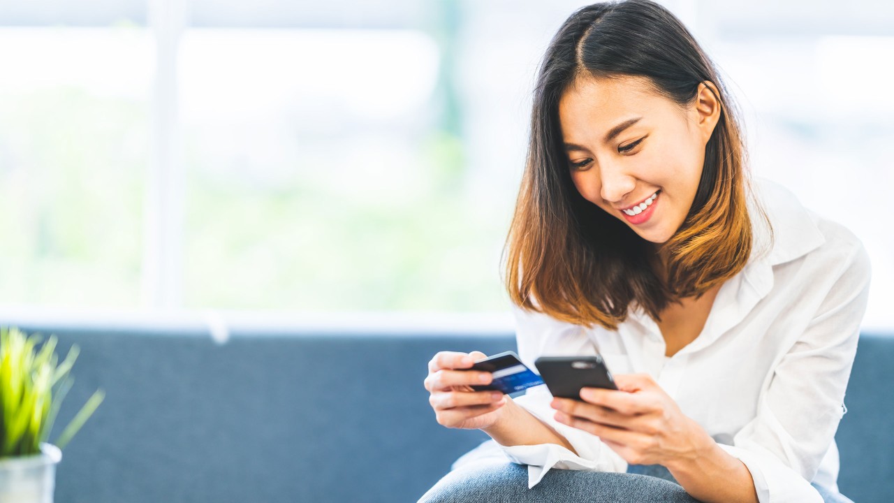 Woman holding credit card and phone; image used for HSBC one-time password ways to bank page.